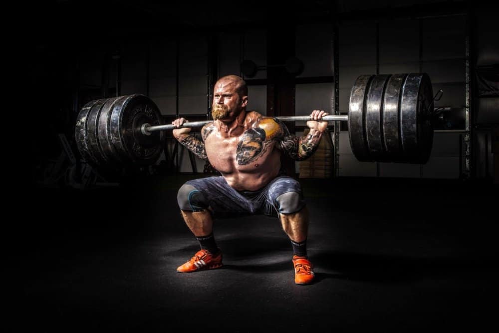 Man squatting heavy barbell in a dimly lit gym