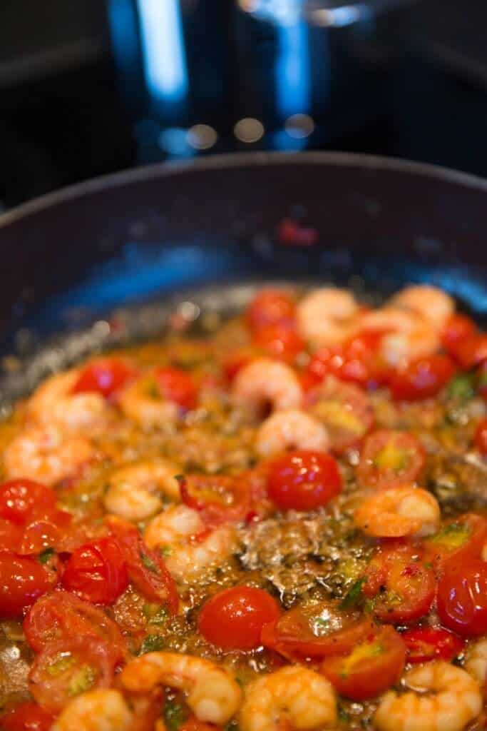 Small shrimp being sauteed in a skillet with cherry tomatoes