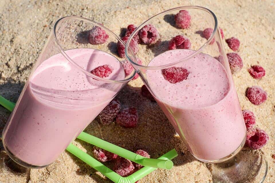 two glass cups on top of sand with a raspberry smoothie inside